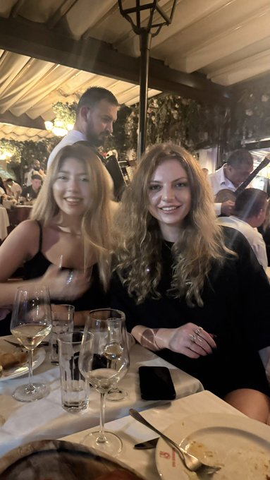 Two smiling women—one with blonde hair and one with curly brown hair—pose together at an elegant dinner table with wine glasses, at what appears to be a cryptocurrency industry networking event. The post's caption celebrates meeting up with fellow women from the crypto community, and the image captures exactly that warm, social moment of connection.