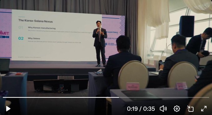 A video screenshot of a man giving a presentation titled 'The Korea-Solana Nexus' with bullet points '01 Why Korean manufacturing' and '02 Why Solana', with an audience seated at tables watching him.