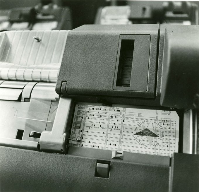 A black-and-white photograph shows a close-up of a vintage computer card reader or output device displaying printed text including "PROGRAM CHECK LIST" and "OUTPUT DATA PROCESS CONTROL".