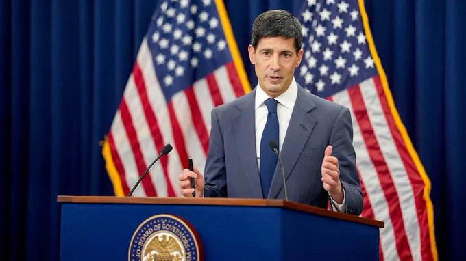 A man in a blue suit stands at a podium labeled "House of Representatives" flanked by American flags, appearing to deliver a press briefing on economic matters. The image ties to the post's commentary about inflation data and muted market reactions, suggesting the official is likely a government spokesperson addressing the latest economic indicators.