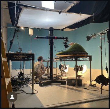 A photography or video production studio setup with overhead lighting rigs, a green screen area, and a person standing at a workstation.