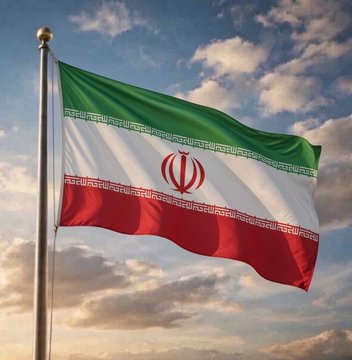 The national flag of Iran (green, white, and red horizontal stripes with the central emblem and decorative borders) waving on a flagpole against a dramatic cloudy sky at sunset.