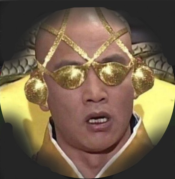 A close-up portrait of a person wearing ornate gold attire, including a headpiece, sunglasses, and earrings, viewed through a circular vignette.