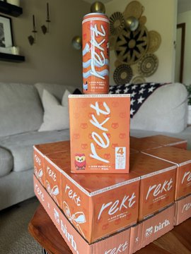 Stacked boxes and a spray can branded 'rekt' displayed in a living room setting.