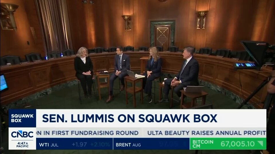 The image shows a group of people sitting around a table, with one person speaking into a microphone. They appear to be engaged in a discussion or panel event related to cryptocurrency regulation. The text "CLARITY ACT IS BEING WRAPPED INTO ONE MASSIVE BILL!" suggests that the topic is being discussed on a national news program, and the focus of the conversation seems to be on the clarity act bill. This bill aims to provide clarity in the crypto space by defining what constitutes cryptocurrency and outlining its legal status. The image captures this moment as it unfolds during the panel discussion or interview.
