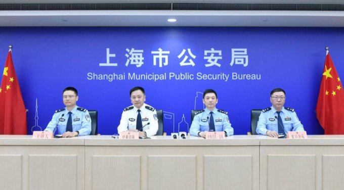 Four officials in police uniforms sit at a table in front of a backdrop reading '上海市公安局 / Shanghai Municipal Public Security Bureau', flanked by two Chinese flags.
