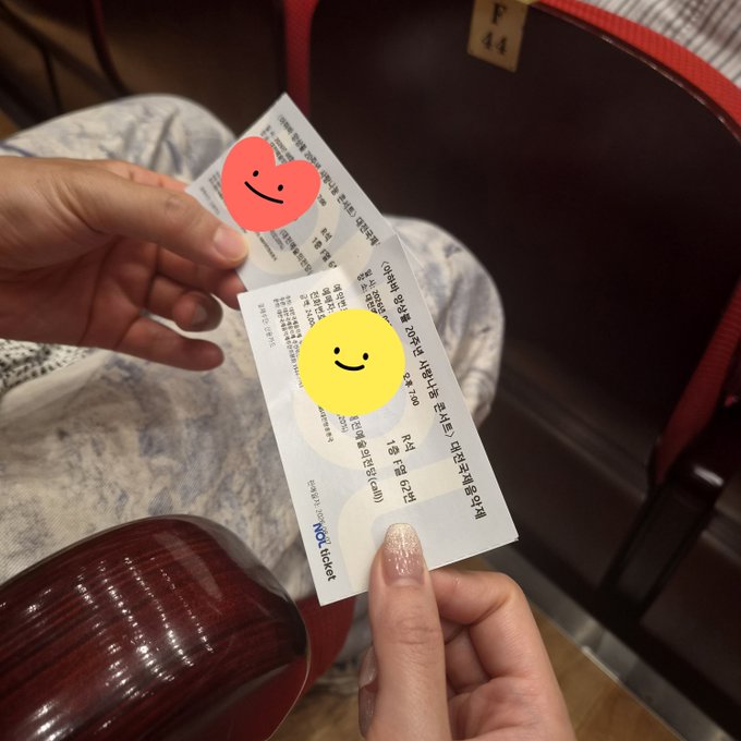 A person holds a WowTicket receipt in Korean, showing partial text 'Rotisserie Chicken' and 'Red Pepper Paste' with smiley face stickers placed over parts of the ticket.