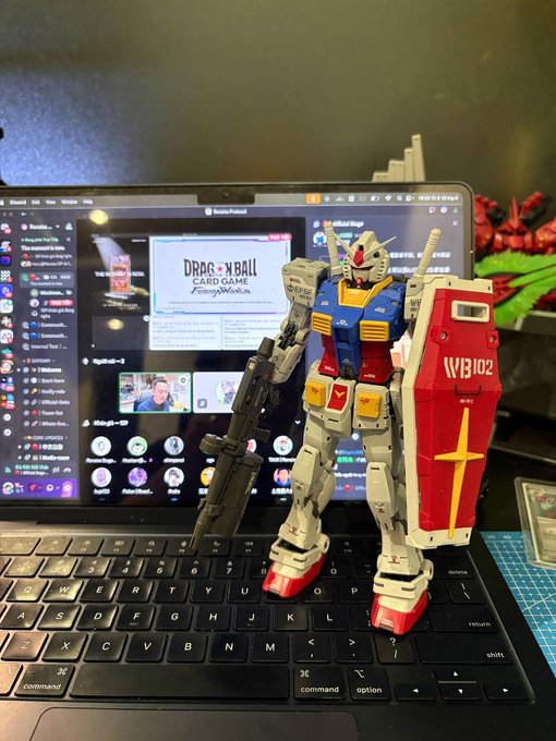 The image features a computer keyboard with a model of a robot standing on top of it, holding a gun. The robot has red and blue armor and is positioned near the center of the keyboard. In the background, there's a monitor displaying a website called "Dr. Ball Game".