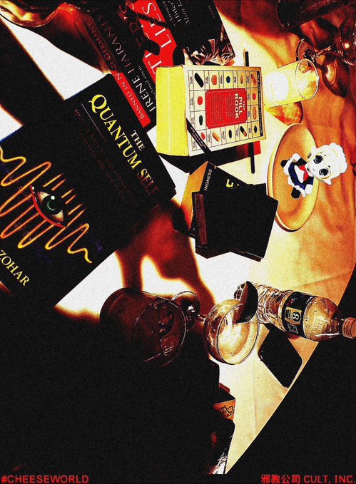An overhead photograph of a table setting featuring a 'The Quantum Self' book, a cigarette box, a panda figurine, a wine bottle, and a glass mug, with the text '#CHEESEWORLD' and '塔教公司 CULT. INC.'.