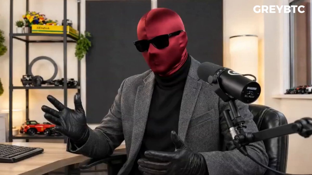 The image features a man wearing a red mask, sunglasses, and a suit jacket while sitting at a desk with a microphone. The background includes a window and various objects such as a keyboard, a car, and a potted plant. The caption reads "Focus on what is in the image and how it relates to the post", which suggests that the image may be related to a discussion or analysis of the content displayed in the caption.