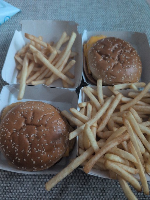 Two sesame seed cheeseburgers and a generous portion of french fries served in paper trays, exemplifying a hearty, indulgent fast-food meal that lives up to the "fatty" description.