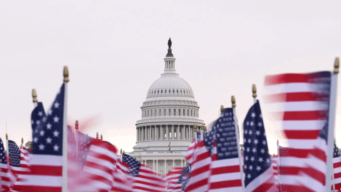 The U.S. Capitol building is shown behind several waving American flags.