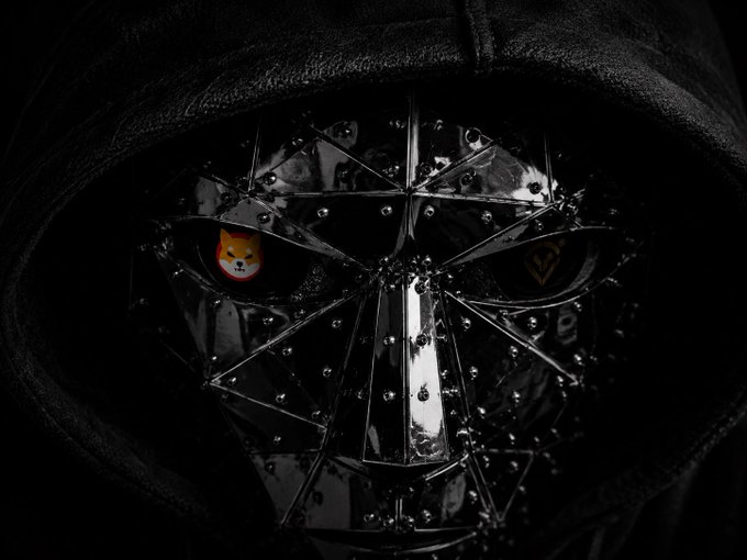 A dark, hooded figure wearing an ornate spiked metal mask with sharp teeth, with two crypto tokens (one featuring a Shiba Inu dog) reflected in the eye slits.