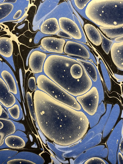 A marbled abstract artwork featuring swirling pools of deep blue, black, and cream colors with scattered speckle details, presented as a limited edition NFT (CE #18/31) on the Tezos blockchain via Objkt for 1.00 $XTZ. The organic, fluid patterns showcase the traditional ebru marbling technique, with the natural, handcrafted appearance reflecting its "nondigital, handmade" description.