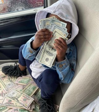 In this image, there are multiple US dollar bills scattered around a child who is sitting comfortably on a chair with his head resting on them. The scene seems to be related to Cryptocurrency trading or financial discussions about Polymarket. The title of the photo suggests that someone has predicted the value of these bills accurately and made $229,913.49 in trades.