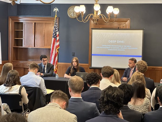 The image shows a group of people gathered around a conference table for a staff lunch meeting at the U.S. Capitol building. The attendees are dressed professionally, with some wearing ties. They appear to be engaged in a discussion about market structure legislation or related topics. A large screen is visible behind them, displaying information relevant to their conversation.

The room has wooden furniture and a blue wall, creating an atmosphere of formality and professionalism. There are several chairs placed around the table, accommodating the attendees. The image also includes text that reads "@lindsayfraser0 joined @solanainstitute's @thecolinmclaren and @Coinbase's @robinrcook to discuss the importance of market structure legislation, U.S. competitiveness, national security," which suggests a connection between the meeting and broader political or economic discussions.