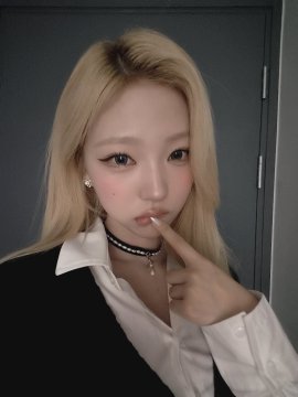 A young woman with blonde hair wearing a black choker and white shirt poses with her finger near her lips.