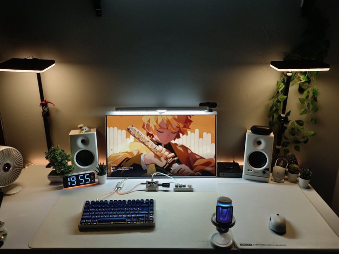 A desk setup features a monitor displaying a Zenitsu (Demon Slayer) wallpaper, a mechanical keyboard, white speakers, a digital clock reading 19:55, and dual lamps with hanging plants.