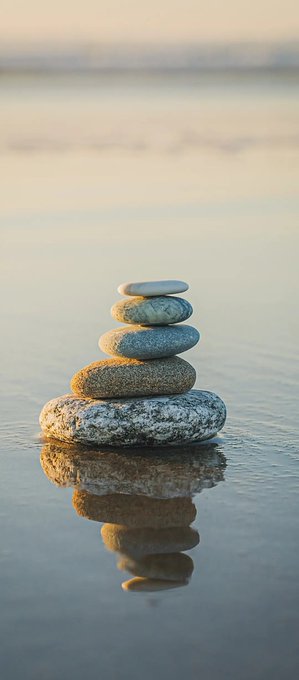 A small stack of five stones is balanced on the surface of a calm body of water, with its reflection visible below.
