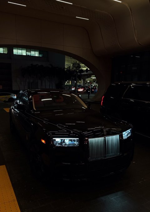 urns of a black Rolls Royce with silver grille and headlights, parked under a curved ceiling, with city lights visible through the windows.