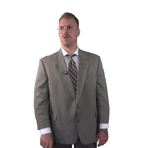 The image features a man wearing glasses, a suit, and a tie standing against a white background. The man appears to be dressed professionally as he poses confidently with his hands at his sides. There are no other people or objects visible in the image, making it seem like an isolated scene focused on the man's attire and expression.