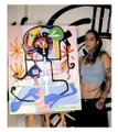 A woman stands beside a large, colorful abstract artwork featuring swirling multicolored shapes, visible text reading "CAVERNA," and blue accents, showcasing the physical piece that is being shared as a 1/1 NFT on SuperRare.