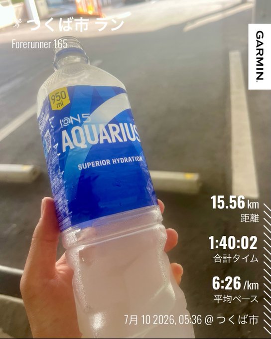 A hand holding an Aquarius Ions sports drink bottle (950ml) after a 15.56 km run in Tsukuba City, with Garmin stats showing 1:40:02 total time and 6:26/km average pace.