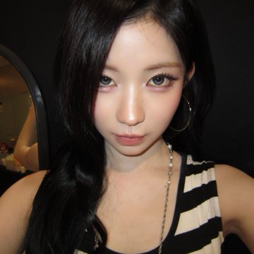 A close-up portrait of a young woman with long dark hair, wearing a striped black and white top and hoop earrings, with dramatic eye makeup and pink lips.