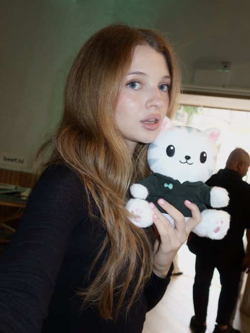 A woman holds up a white plush cat toy dressed in a black hoodie.