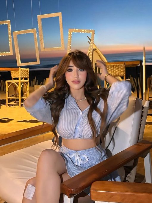 A young woman with long wavy brown hair sits on a beachside lounge chair at sunset, wearing a blue-and-white striped crop top and matching shorts, with her hands raised to her hair. The post appears to be a reflective, philosophical message about the evolving nature of reputation in Web3, suggesting the image serves as a personal, relatable visual to accompany the more analytical text.