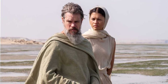 A bearded man in a green robe and a woman wearing a white head covering stand together in a shallow, desert-like landscape, evoking the ancient Mediterranean setting of Homer's Odyssey. The post humorously conflates Christopher Nolan's upcoming "The Odyssey" with Jack Dorsey's attempts to reclaim Twitter's CEO role, with the image's solemn, epic mood ironically amplifying the critique of Nolan "turning one of the most epic stories ever told" into something grittier and presumably less compelling.