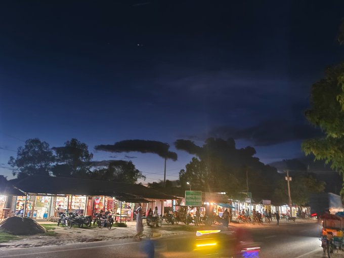 A bustling night street scene shows illuminated shops, parked motorcycles, and silhouetted trees under a dark blue sky, with vehicles in motion creating light trails on the road. The vibrant roadside activity contrasts with the tech-focused post about quantum computing and Web3, illustrating a lively everyday environment rather than the futuristic digital theme being discussed.