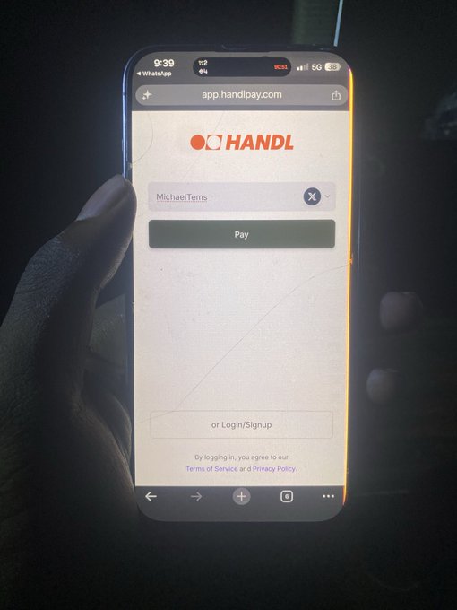 A hand holds a smartphone displaying the HANDL app (app.handlpay.com) with a payment field showing 'MichaelTems' above a Pay button.