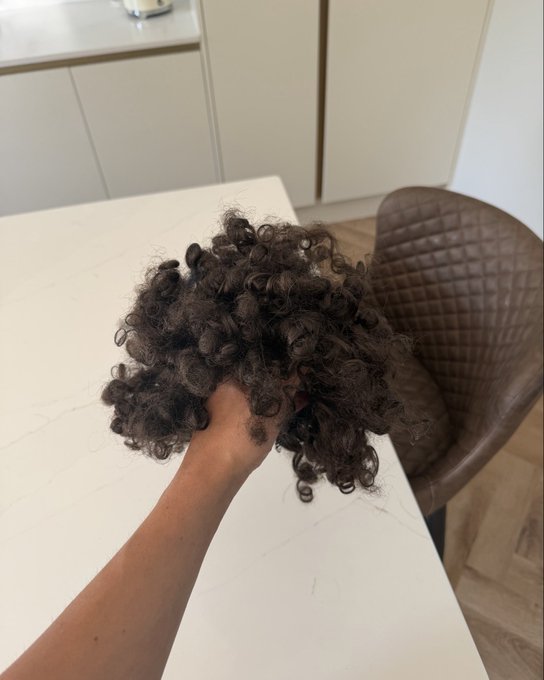 A person holding a bundle of curly dark brown hair over a white kitchen countertop.