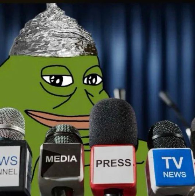 A Pepe the Frog meme wearing a tinfoil hat, sitting at a press conference table with multiple microphones labeled "MEDIA", "PRESS", and "TV NEWS" in front of a blue curtain.