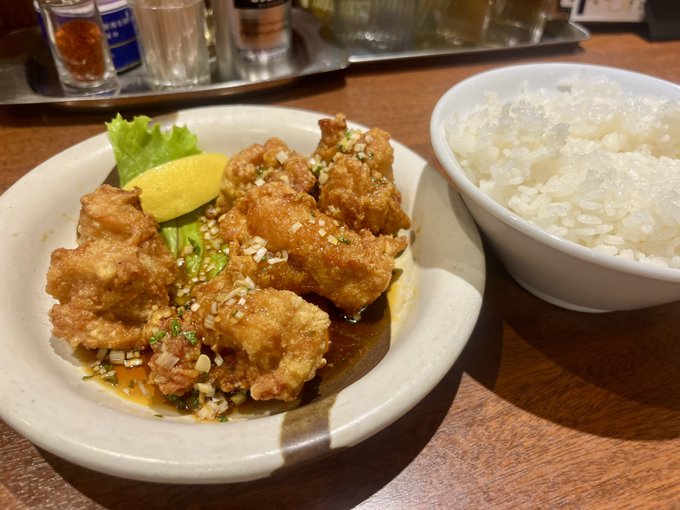 A plate of golden-brown karaage (Japanese fried chicken) garnished with chopped green onions and served with a lemon wedge and lettuce, accompanied by a bowl of fluffy white rice—matching the post's praise of Yukimura's karaage sauce and the sentiment that Japanese people should choose authentic Japanese fried chicken over KFC.