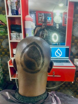 A man sits in a barbershop chair with a large triangular geometric design shaved into the back of his head.