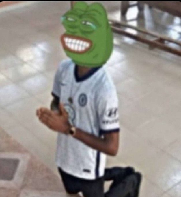 A young person kneels on a tiled floor wearing a white sports jersey with visible logos, while their head is digitally replaced with the grinning "Dat Boi" Pepe frog meme face, reacting to the post about dropping "illeri don drop 2 articles" and begging "@ansem" for an airdrop.