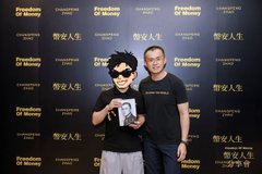 Two people posing at a 'Freedom Of Money' event backdrop with Chinese text '幣促人生'; one wears sunglasses and holds an award/box, the other is in a black shirt.