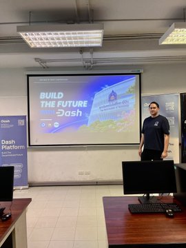 A man giving a presentation in an office setting, with a projector screen displaying the text "BUILD THE FUTURE WITH Dash".