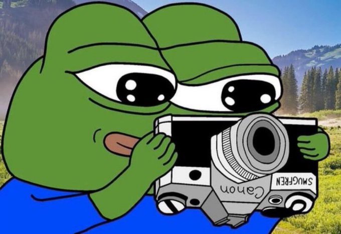 The image features a cartoon frog holding a camera with its mouth while standing in front of a mountain landscape. The frog appears to be taking a picture or recording something interesting happening around them, possibly capturing the beauty of nature or an event occurring nearby.