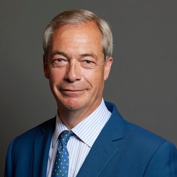 A professional headshot of a middle-aged man with graying hair, wearing a blue suit jacket, striped shirt, and blue patterned tie, photographed against a dark gray background—likely depicting Nigel Farage in connection with his support of the Stack BTC acquisition proposal for Direct Bullion.