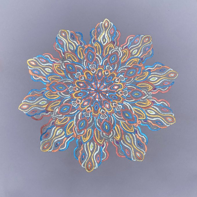 A vibrant, symmetrical mandala drawing created with colored pencils in shades of blue, red, orange, yellow, and white against a gray background.