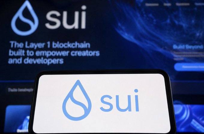 A smartphone displaying the Sui blockchain logo in front of a larger screen showing 'sui - The Layer 1 blockchain built to empower creators and developers'.