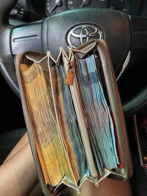 An open, overflowing brown zippered wallet stuffed with papers and cards is held in front of a Toyota steering wheel, manifesting a similarly packed wallet in August.