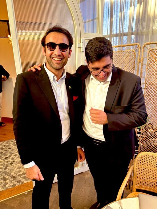Two men in suits smile warmly while posing together at what appears to be a formal event, with one wearing dark sunglasses and the other sporting eyeglasses and adjusting his jacket in mid-laugh. The celebratory, amicable vibe of the photo complements the post's optimistic tone about regulatory progress in the space, capturing the kind of in-person networking moment that makes "easier conversations for investors and partners" a reality.