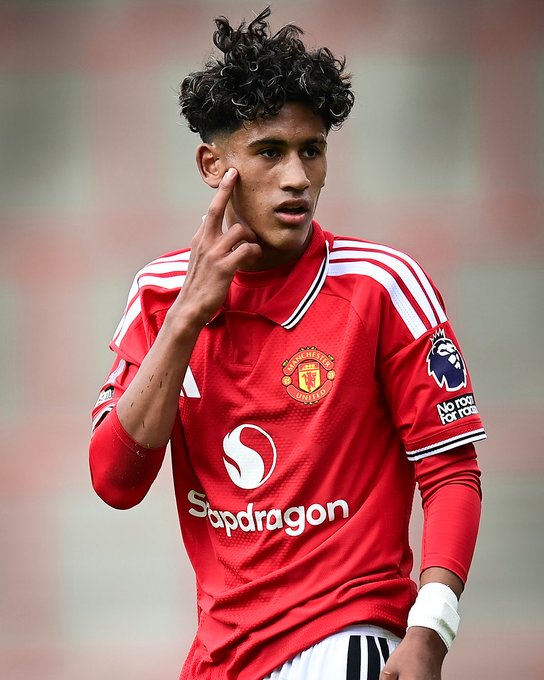 A teenager wearing Manchester United's red home kit with "Snapdragon" sponsor text and the No Room For Racism Premier League badge looks off-camera, making a two-finger gesture near his face. The image connects to the caption about where JJ Gabriel, a highly touted young Manchester United prospect, might transfer in his career.