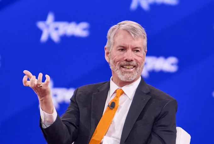 Michael Saylor, founder of Strategy (formerly MicroStrategy), speaks animatedly at a CPAC event against a blue star-spangled backdrop, gesturing with his hand as he addresses the audience. The image accompanies news that his company sold $603M worth of MSTR shares to purchase $370M in Bitcoin while boosting cash reserves to $6.71B.