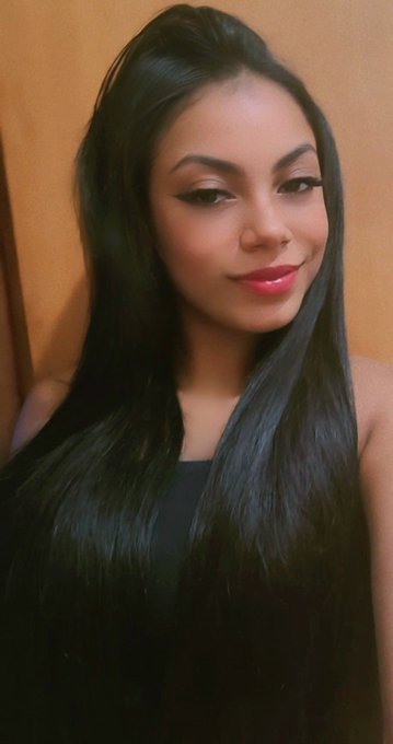 A selfie portrait of a woman with long black hair, dramatic eye makeup, and red lipstick.