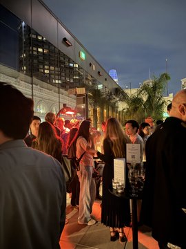 A nighttime outdoor scene showing a crowd of people gathered on a city sidewalk, with a "VALET PARKING" sign visible in the foreground.
